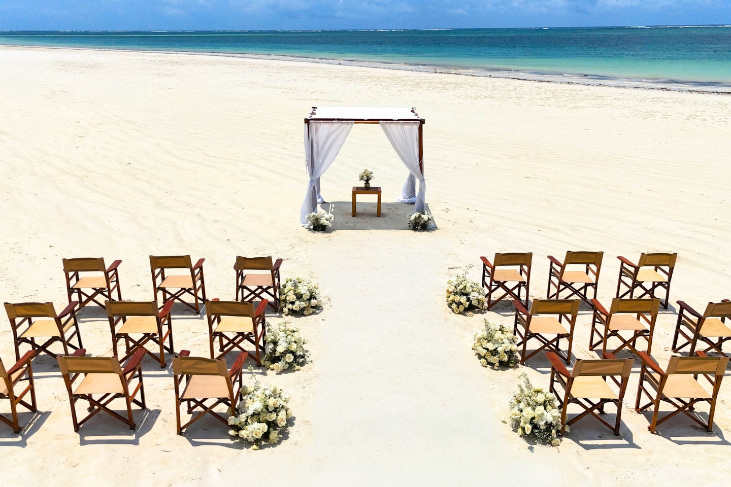 Aerial view of a beach wedding ceremony with wooden chairs and white flowers
