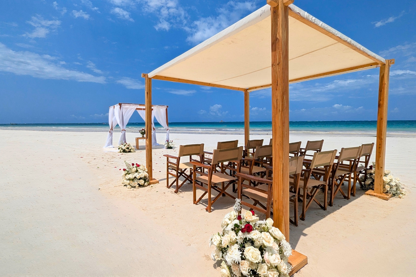 Wooden chairs and white fabric canopies arranged for a wedding on Diani Beach beside the Indian Ocean.