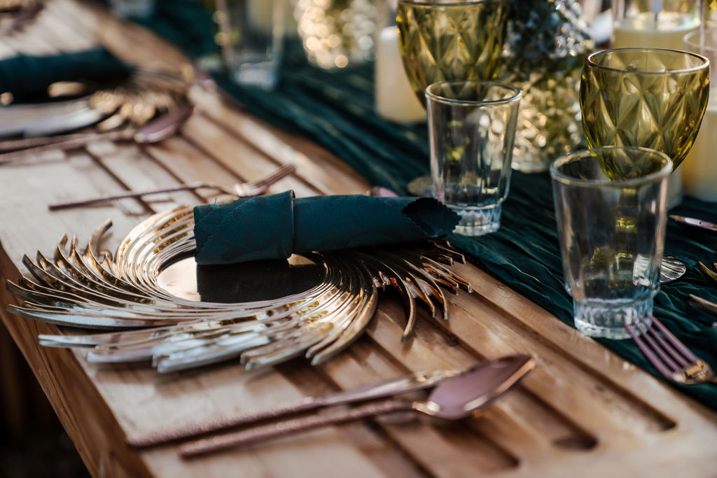 Elegant event table setting with green linen, textured glassware and decorative plates on a wooden table.