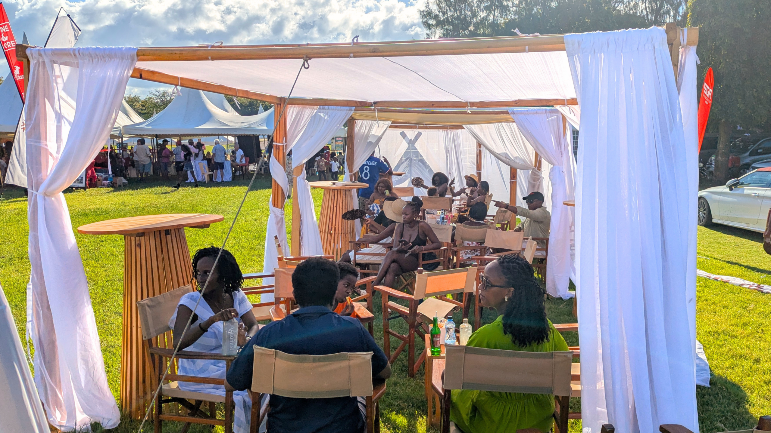 Guests seated beneath white canopies using wooden event furniture